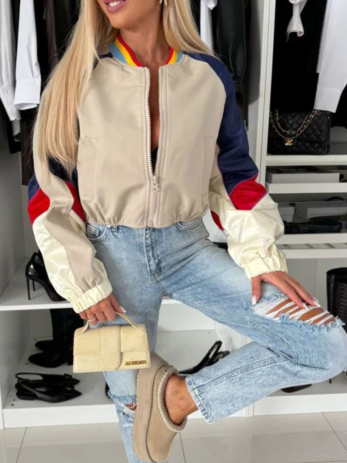 Beige cropped bomber jacket with colorblock sleeves and striped collar, zipped front.