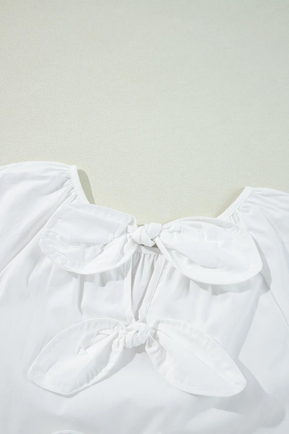 White babydoll blouse with square neckline and two front bow details.