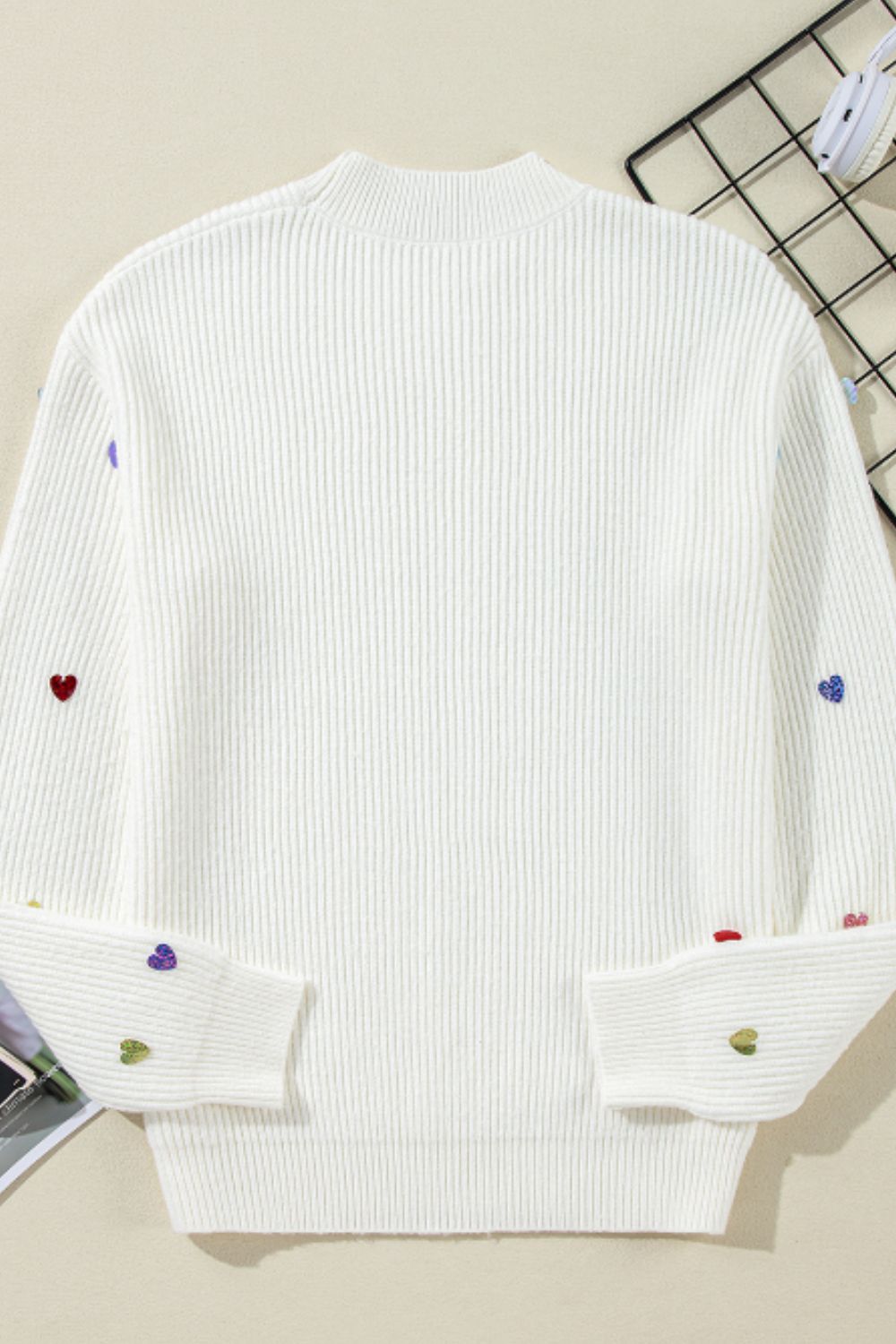 White ribbed knit sweater with embroidered colorful hearts on sleeves and hem.