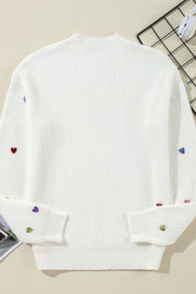 White ribbed knit sweater with embroidered colorful hearts on sleeves and hem.