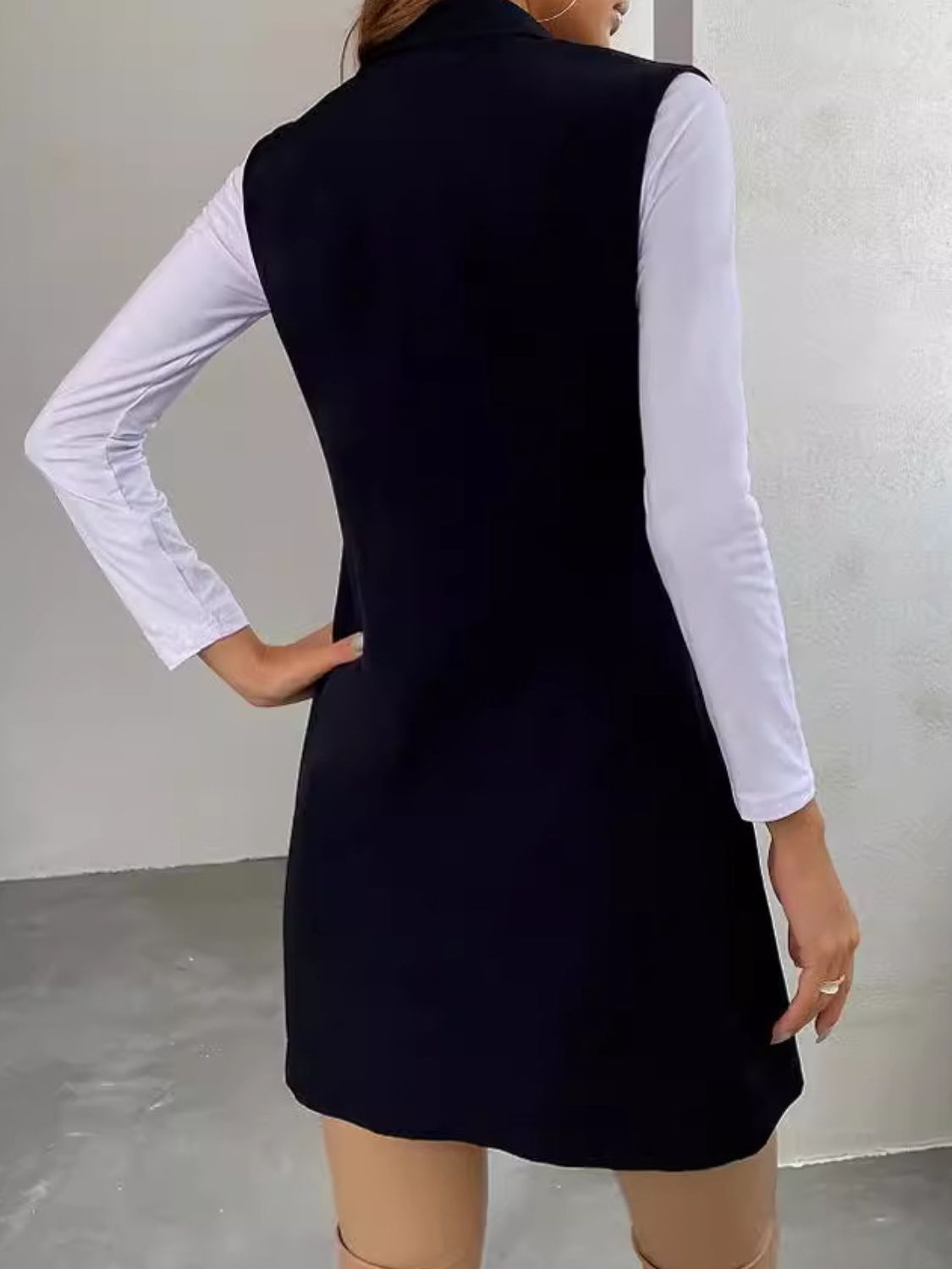 Black draped lapel vest with asymmetric hemline worn over a white long-sleeve top.