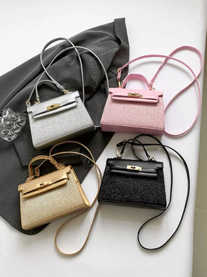 Glitter textured mini crossbody bags in gold, pink, silver, and black with top handles and shoulder straps.