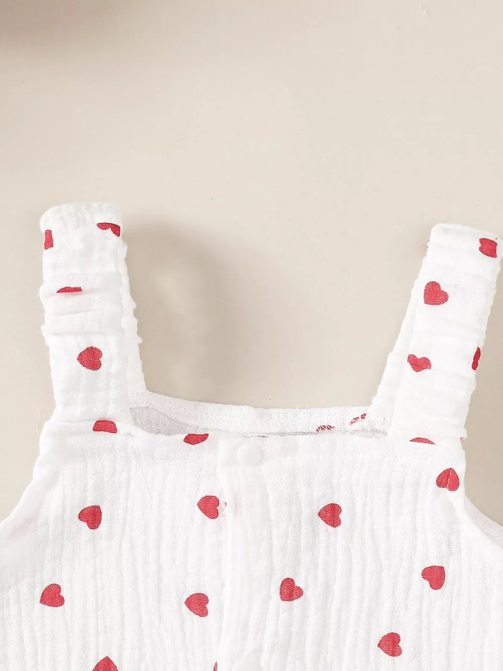 White baby romper with red hearts, ruffled straps, and button front.