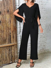 Black cape sleeve wrap jumpsuit with tie waist and wide leg pants.