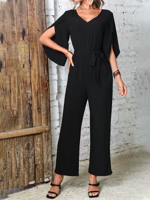 Black cape sleeve wrap jumpsuit with tie waist and wide leg pants.