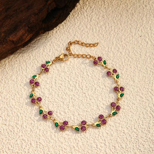 Gold-plated cherry cluster bracelet with purple gems and green leaf accents.