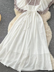 White embroidered V-neck maxi dress with tie waist and flowing skirt.