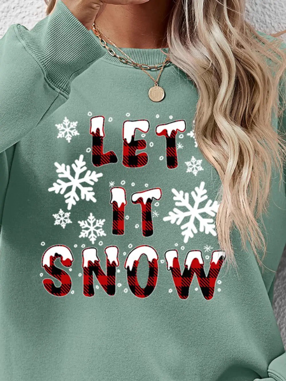 Sage crewneck sweatshirt with "Let It Snow" graphic in buffalo plaid and snowflakes.