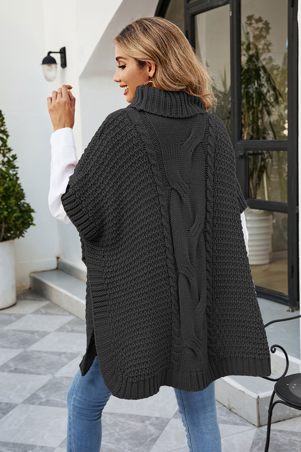 Black cable knit turtleneck poncho with side slits and a textured knit pattern.