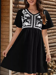 Black V-neck mini dress with white floral embroidery on bodice and short sleeves.