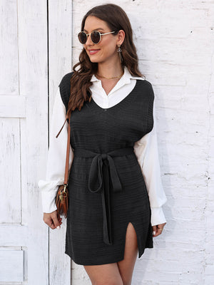 Black knit vest dress with V-neck, tie waist, and side slit, layered over a white shirt.
