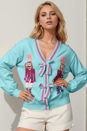 Cerulean acrylic cardigan with nutcracker embellishments and pink trim bows.