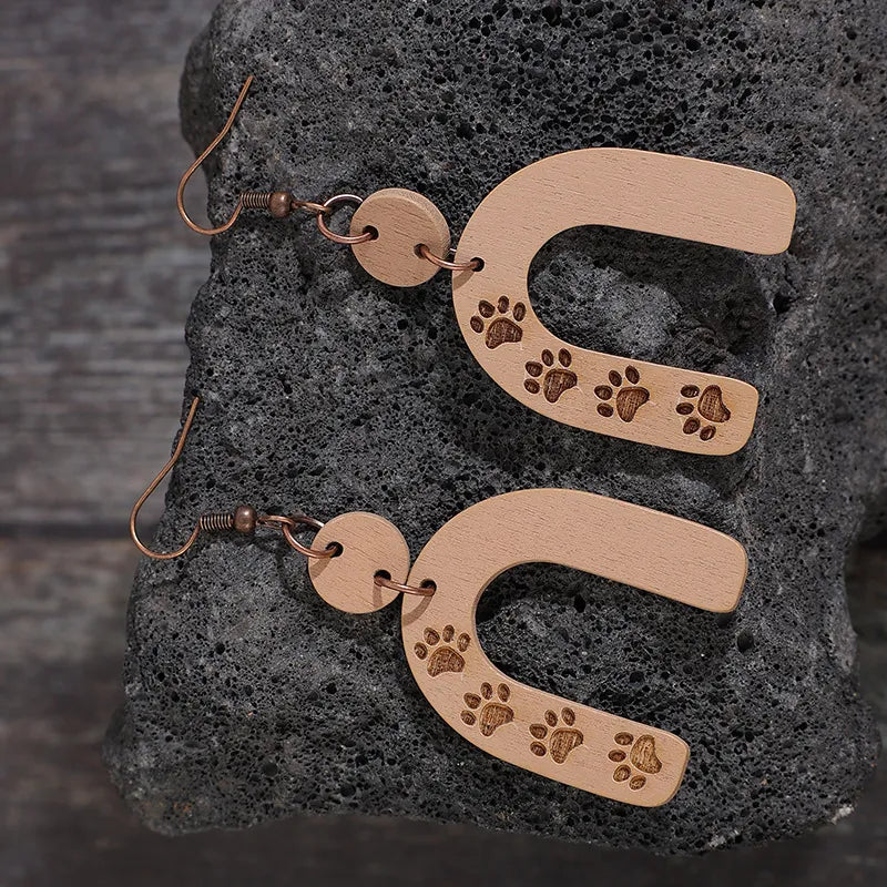Wooden arch earrings in camel with engraved paw prints and copper hooks.