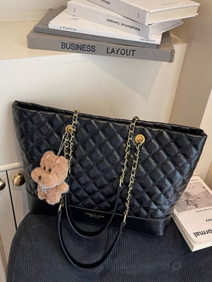 Black quilted shoulder bag with gold chain straps and a teddy bear charm