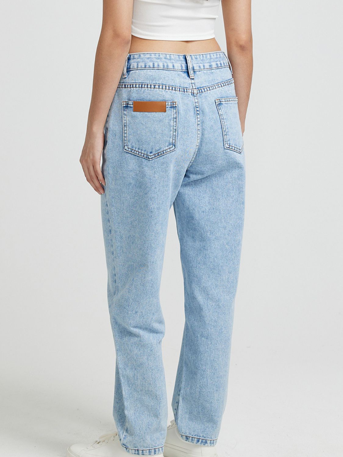 Light wash denim jeans with high rise and buttoned closure, featuring a brown leather patch detail on the back pocket.