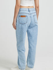 Light wash denim jeans with high rise and buttoned closure, featuring a brown leather patch detail on the back pocket.