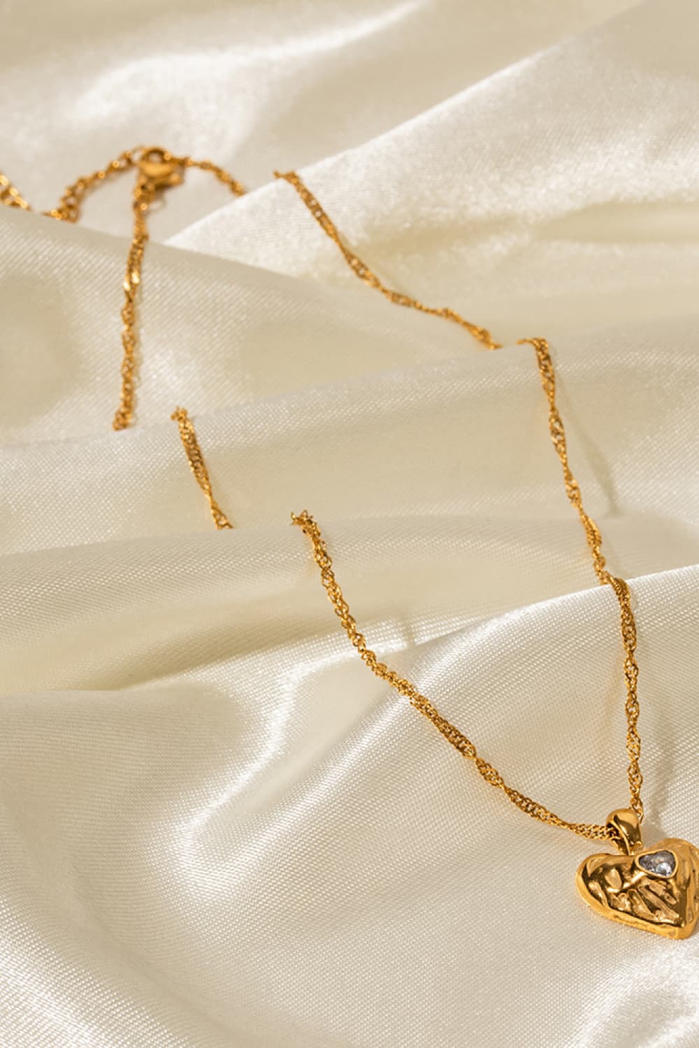 Gold textured heart pendant necklace with a clear stone detail on a delicate chain.