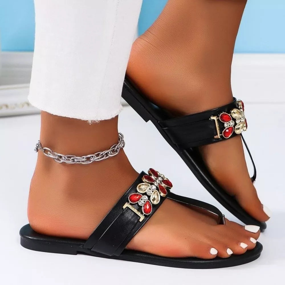 Black jeweled toe-post flat sandals with red and gold flower embellishments and a silver ankle chain.