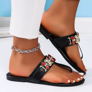 Black jeweled toe-post flat sandals with red and gold flower embellishments and a silver ankle chain.