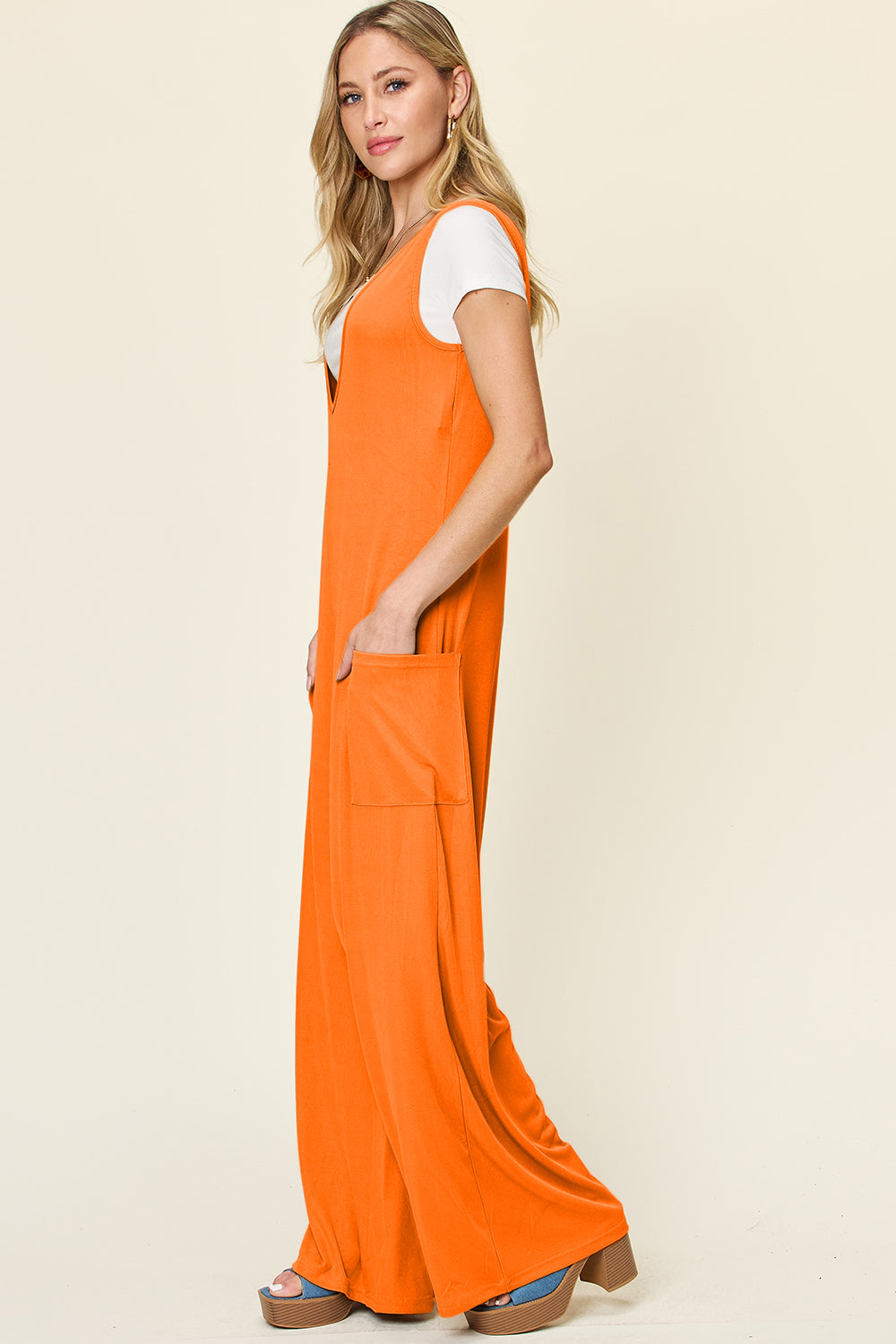 Tangerine wide-leg jumpsuit with deep V-neck and front pockets, styled over a white tee.