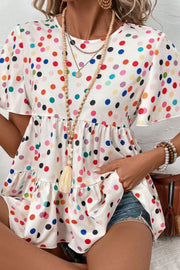White polka dot tiered babydoll blouse with flutter sleeves and tassel necklace.