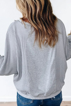 Gray waffle knit top with fringe trim detail, long sleeves, and a relaxed fit.