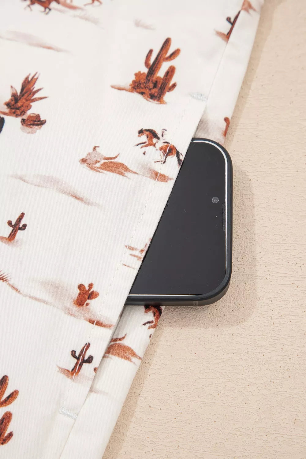 Desert Motif Adjustable Jumpsuit in beige cotton with cactus and horse print, showing a side pocket with a phone.