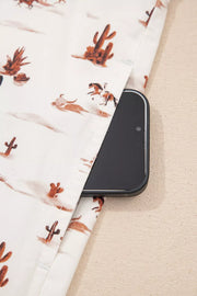 Desert Motif Adjustable Jumpsuit in beige cotton with cactus and horse print, showing a side pocket with a phone.