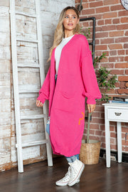 Pink maxi knit cardigan with pockets and an orange peace sign detail.