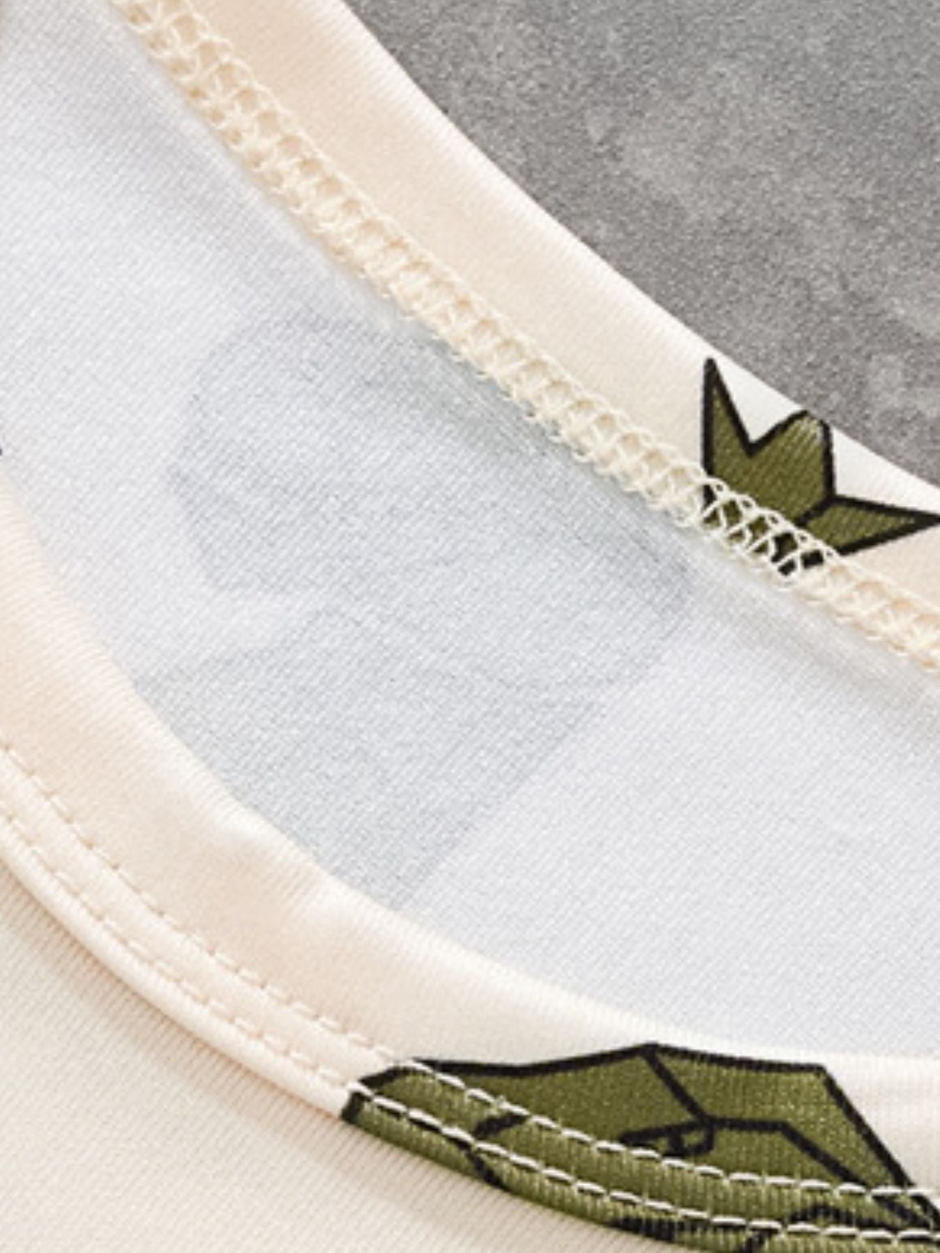 Toddler tee with dinosaur print and cream trim, showing neckline detail.
