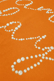 Orange crewneck sweatshirt with pearl embellishments forming a design.