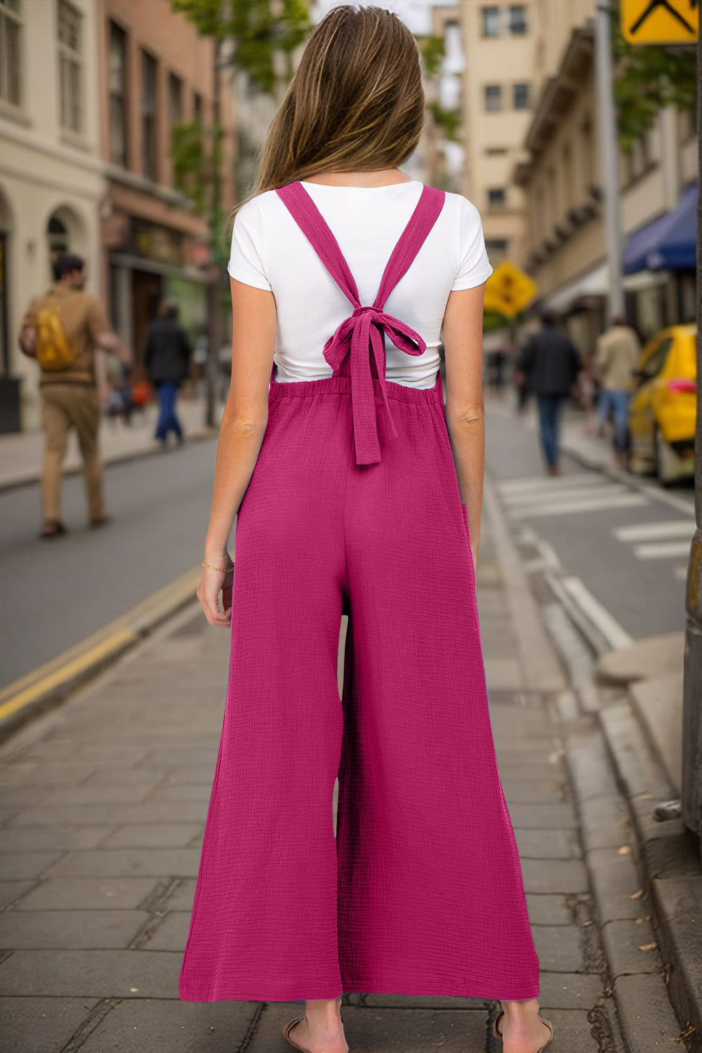 Gathered bib wide-leg jumpsuit in hot pink with tie-back straps and textured fabric.