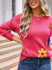 Pink knit sweater with embroidered flower appliqués and blue sleeve details.