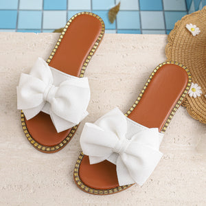 White bowknot slide sandals with brown soles and gold trim detail.