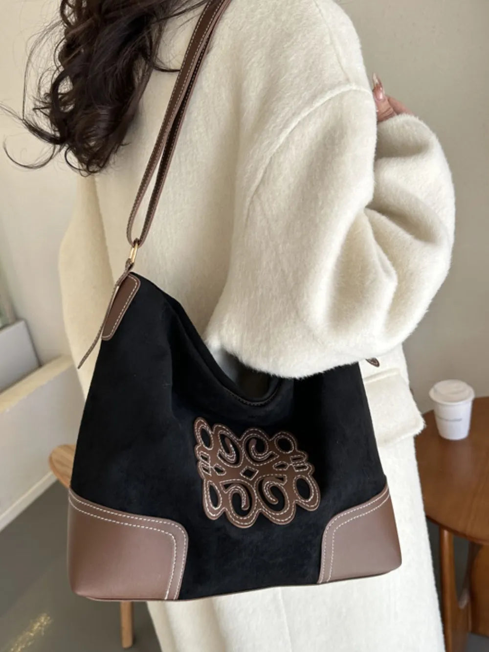 Black suede hobo bag with brown leather trim and appliqué detail, contrast stitching.