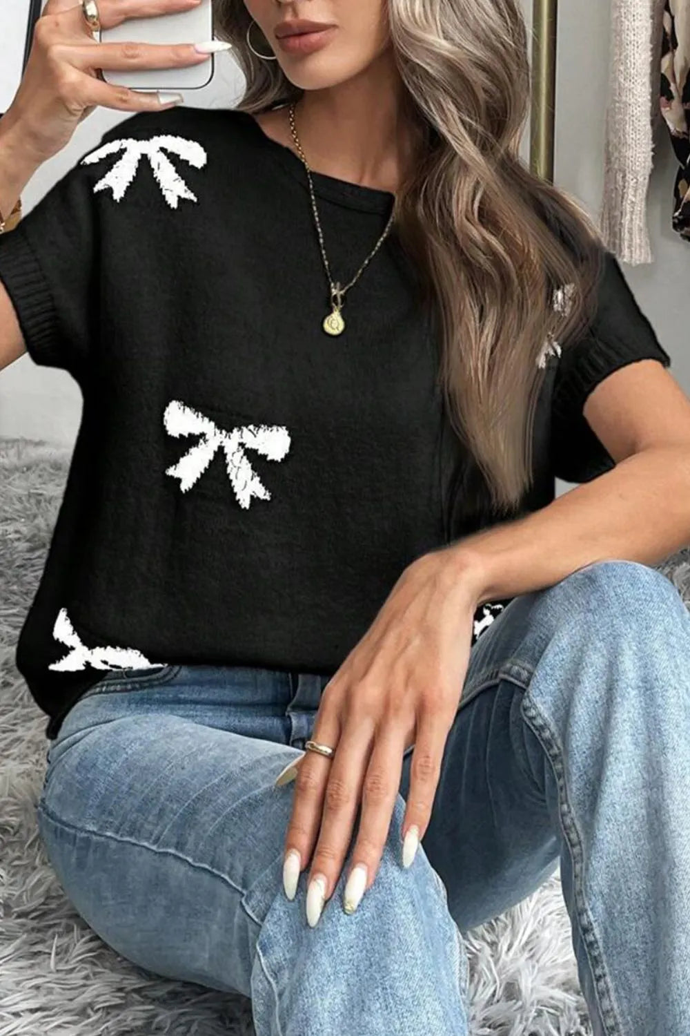 Black knit tunic with white bow motif pattern, short sleeves, and crew neck.