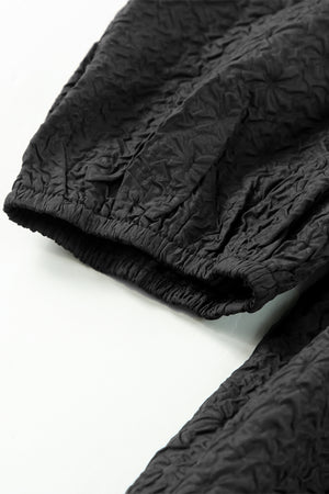 Black textured peplum top with petal sleeves and elastic cuffs.