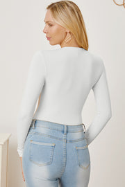 White ribbed long sleeve bodysuit with plunge neckline, styled with light wash jeans.