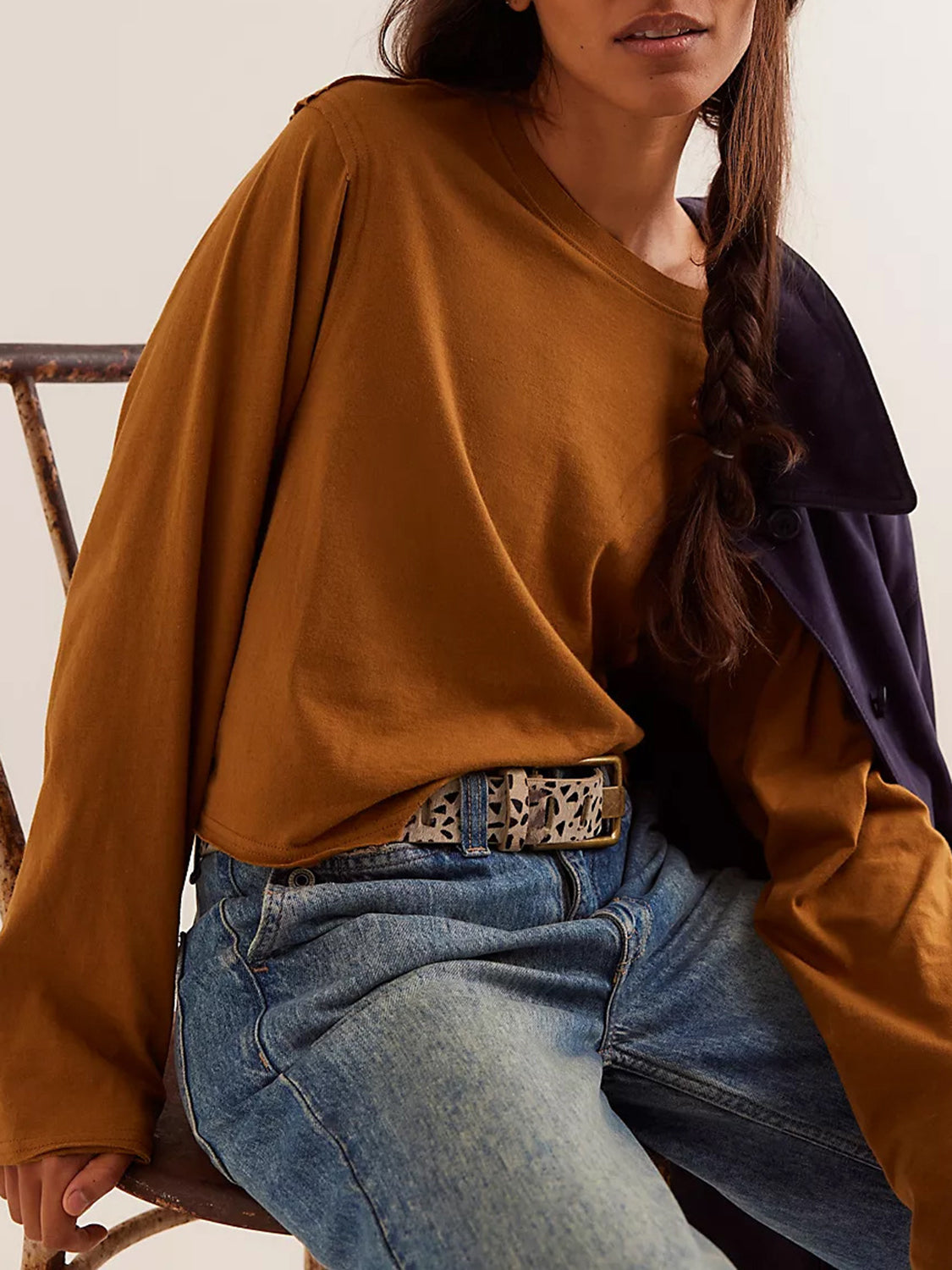 Caramel long sleeve crop top with raw hem detail, styled with jeans and a patterned belt.