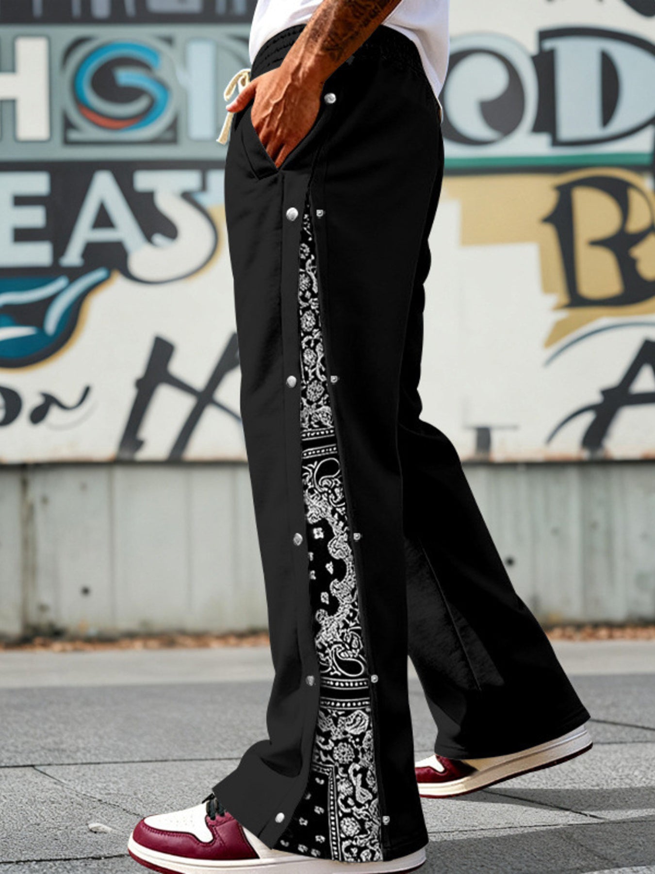 Black sweatpants with wide legs, side snaps, and paisley print detail.