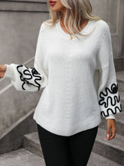White voluminous knit sweater with black embroidered sleeves and a V-neck.