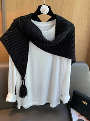 Black chunky knit scarf accessory with tassel detail, draped over a white long-sleeve shirt.
