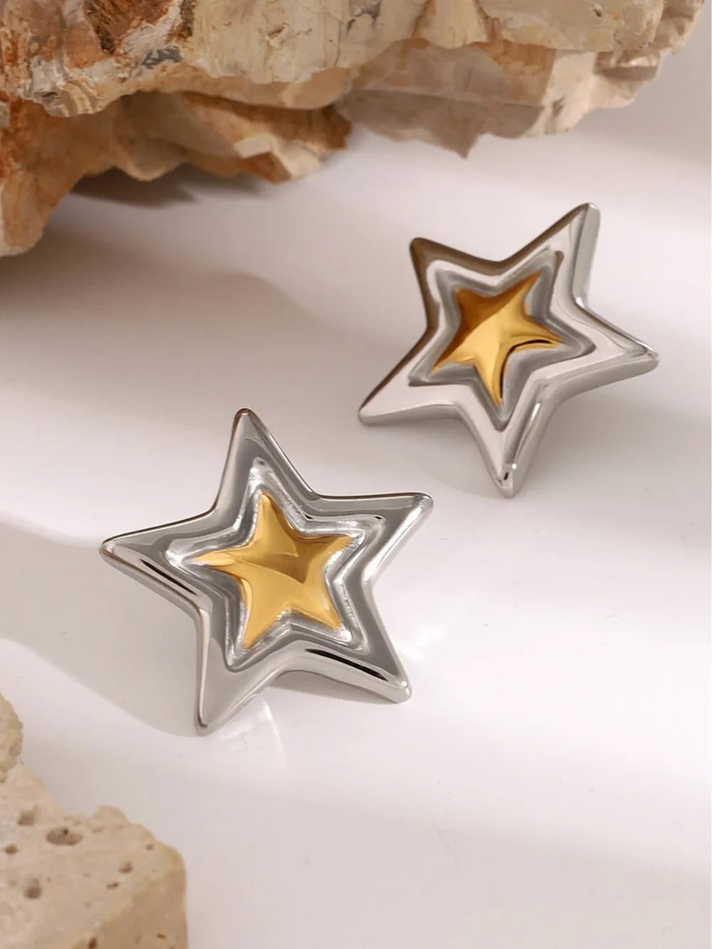 Sculpted starburst stud earrings in silver and gold feature layered star shapes.