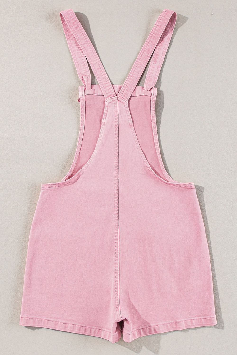 Blush pink denim short overalls with adjustable straps and a casual cut.