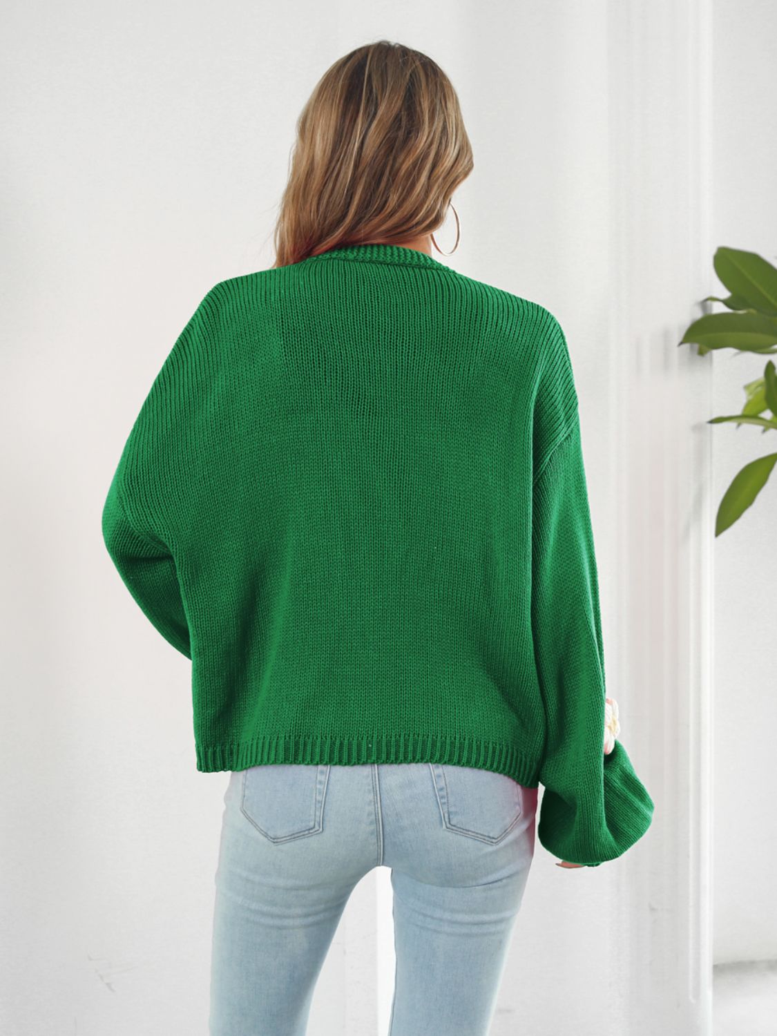 Green knit cardigan with balloon sleeves and floral appliqué detail.