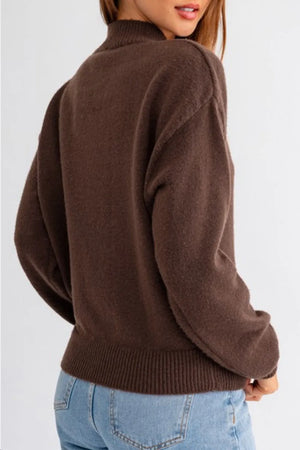Brown knit mock neck sweater with ribbed cuffs and hem, styled with jeans.