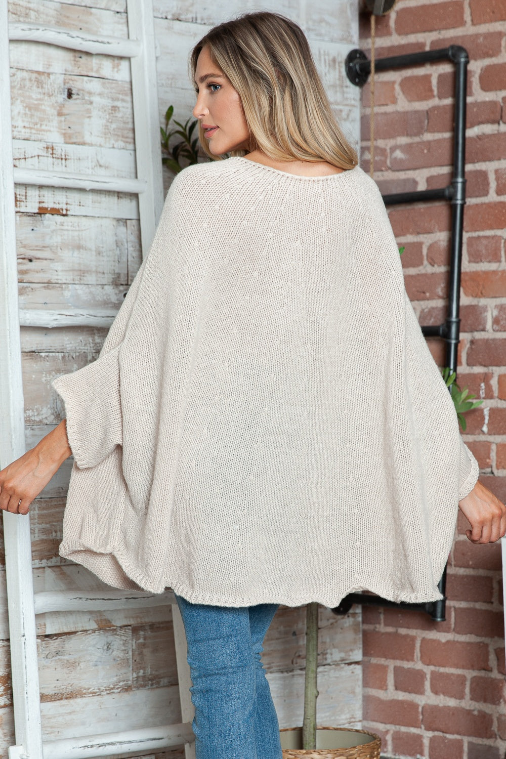 Cream knit sweater with cape sleeves and a relaxed fit, styled with jeans.