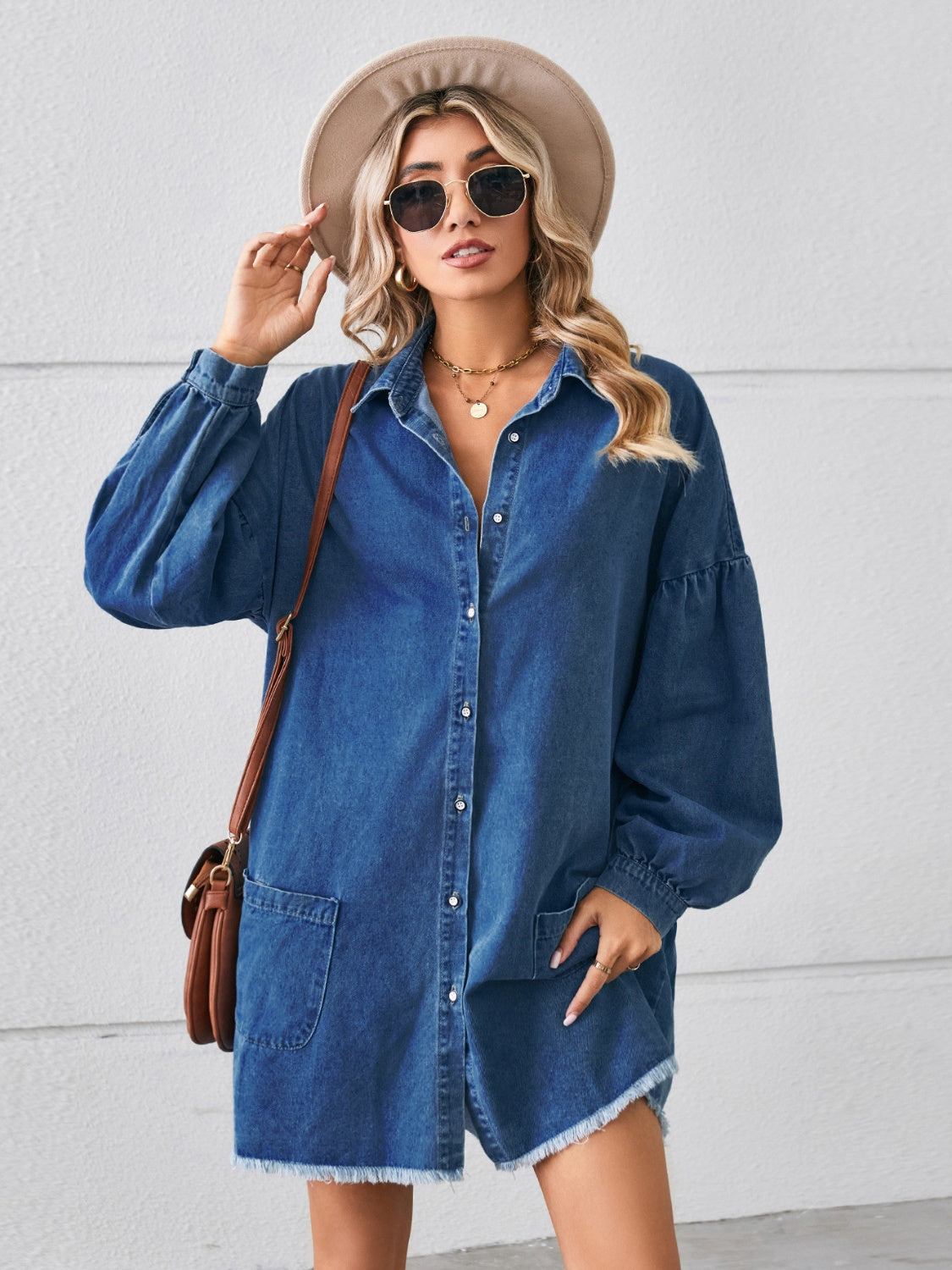 Denim shirtdress in dark blue with voluminous sleeves, button front, chest pockets, and frayed hem.