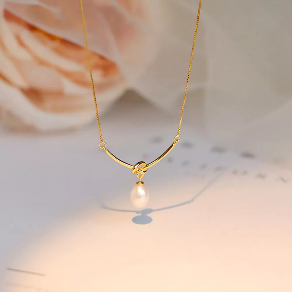 Gold necklace with curved bar, knot detail, and pearl pendant.