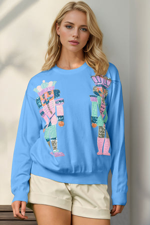 Sky blue crewneck sweater with colorful nutcracker appliqué, 100% polyester.